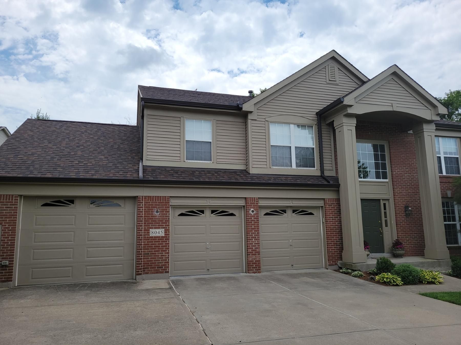 A large brick house with three garage doors and a roof.