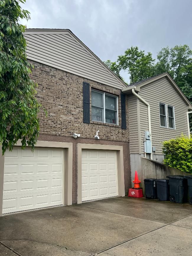 A house with two garage doors and a lot of trash cans in front of it.