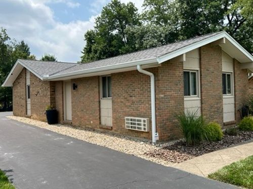 A brick house with a gray roof and white trim is sitting on the side of a road.