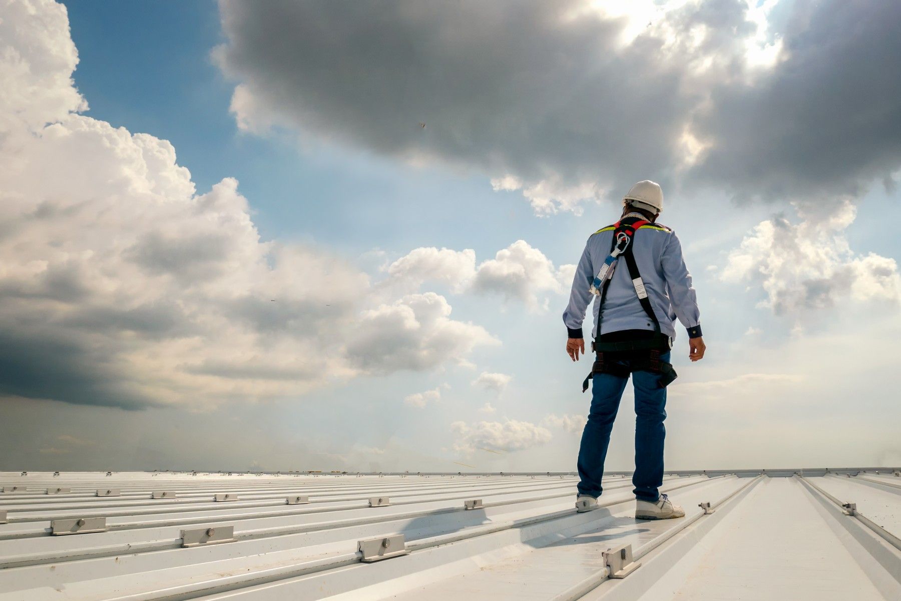 A man is standing on top of a white roof.
