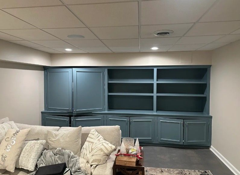 Blue built-in cabinets and shelves in a basement living room beside a cream sofa.