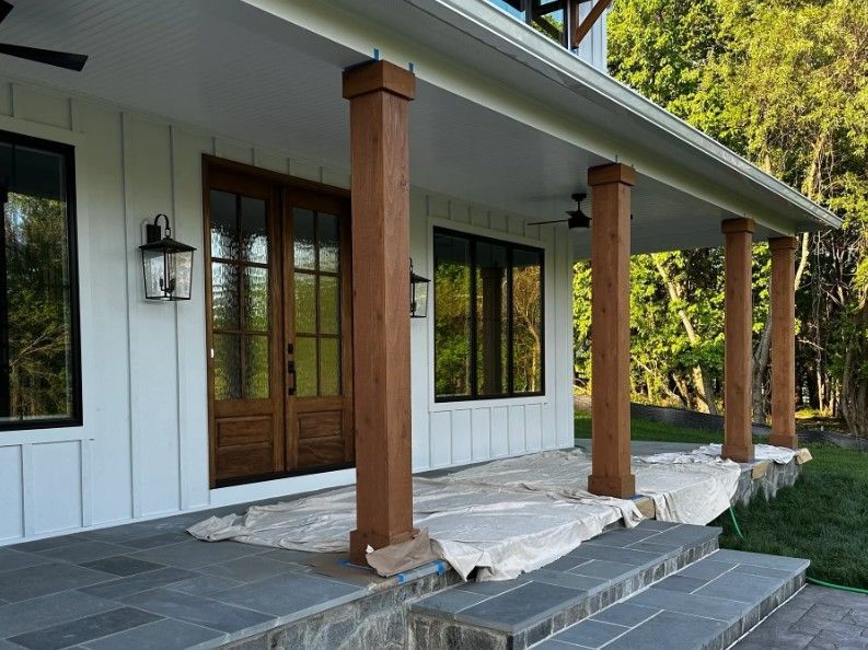 Front porch with white siding, dark stone steps, and wood columns, with protective coverings on the ground.