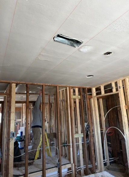 Interior under construction with exposed wood framing and a damaged ceiling vent opening