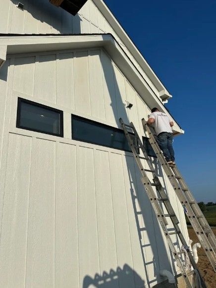 Worker on a ladder painting the exterior of a white house beneath a blue sky