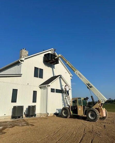White barn under repair with a telescopic lift reaching the roof on a dirt lot under a clear blue sky