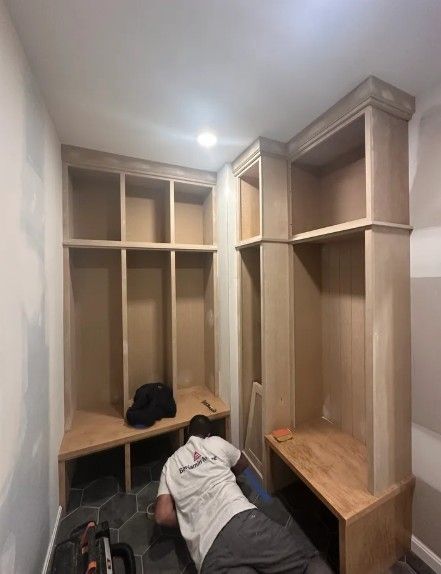 Person kneeling in a walk-in closet, assembling wooden built-in shelving and benches.