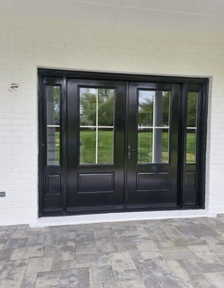 Black double front doors with glass panes in a white exterior wall, opening to a covered patio.