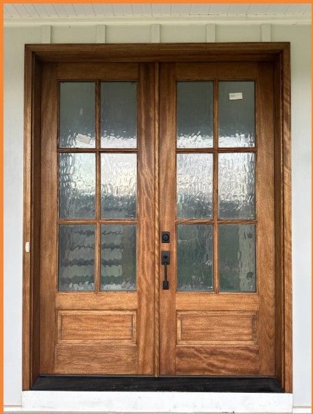 Wooden double front doors with frosted glass panels and black hardware under a porch overhang
