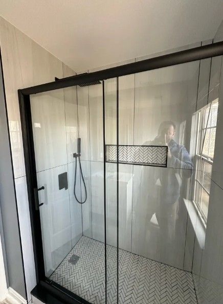 Modern glass shower enclosure with black frame, white tile walls, and a built-in niche shelf