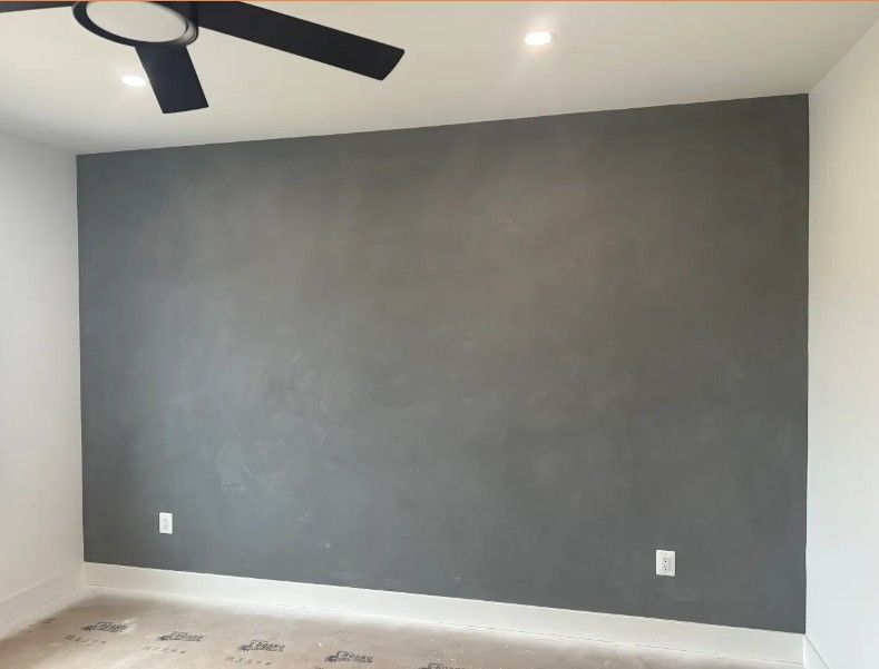 Empty room with dark gray accent wall, white walls, and black ceiling fan.