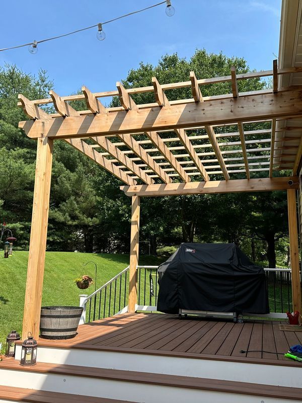 Wooden backyard pergola over a deck with string lights, potted plants, and a covered grill.