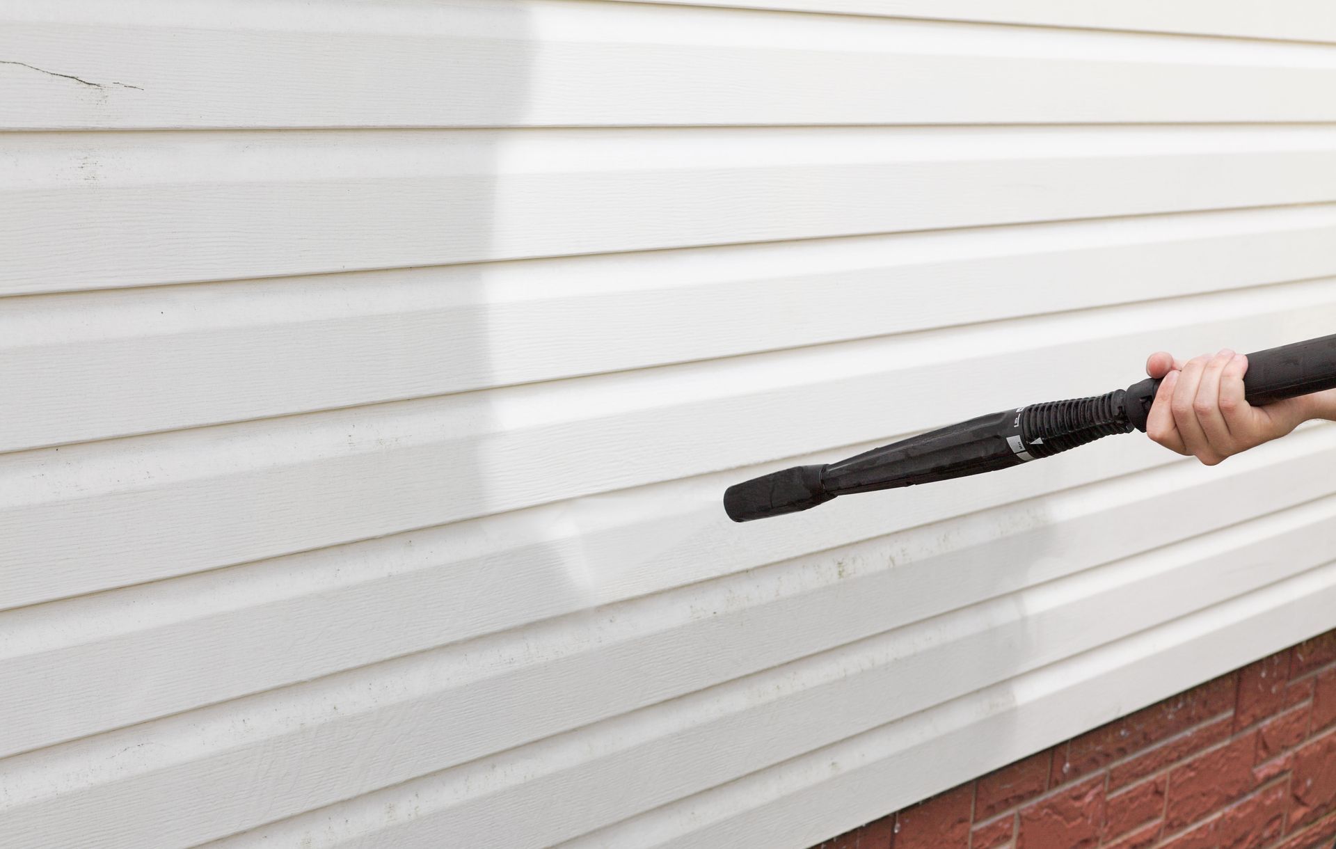 Person pressure-washing a white house wall with a black wand