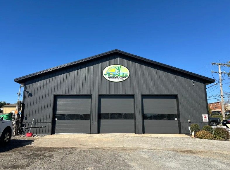 Black industrial building with three garage doors and an oval sign under a clear blue sky