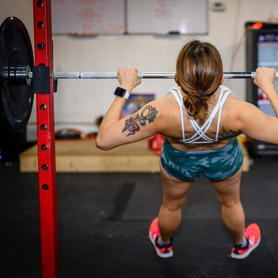 A woman with a tattoo on her arm is squatting with a barbell