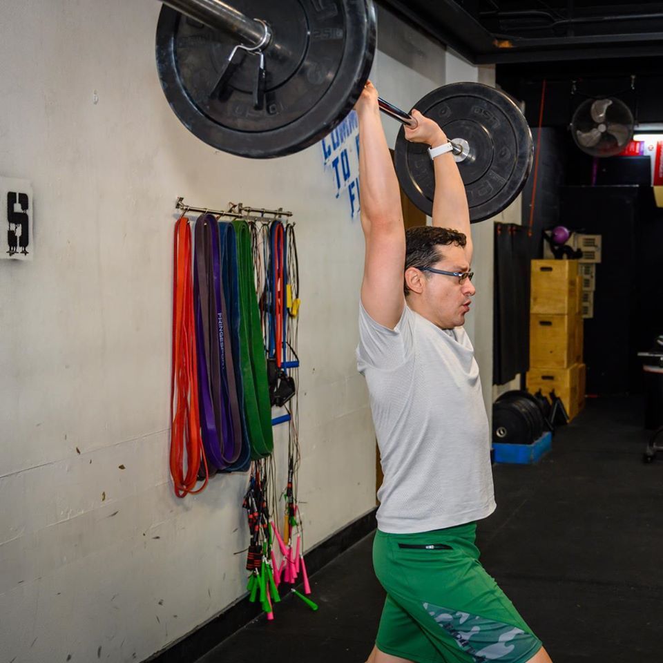 A man is lifting a barbell over his head in a gym
