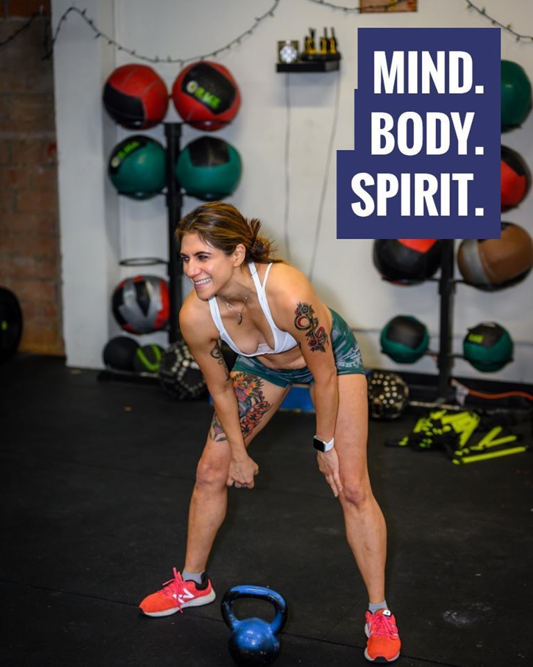 A woman is lifting a kettlebell in a gym with a sign that says mind body spirit