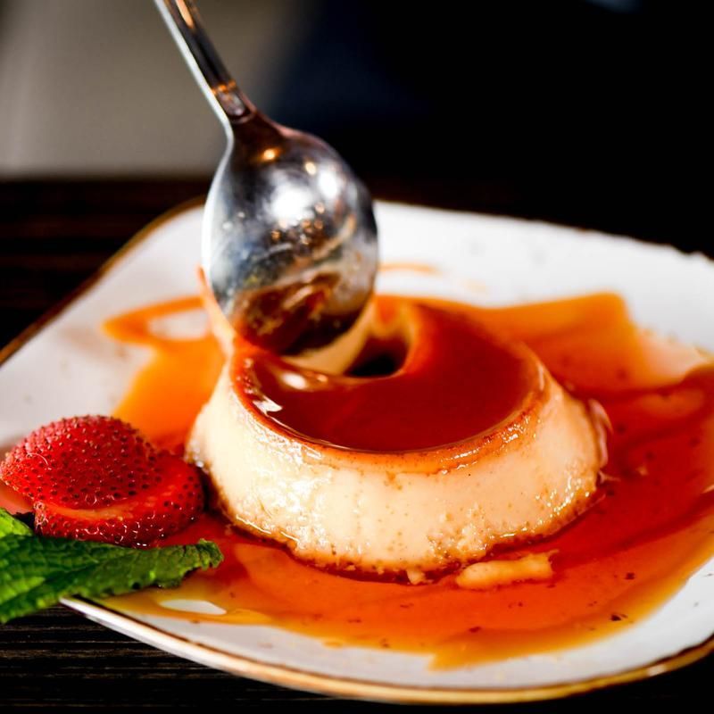 A white plate topped with a flan and strawberries with a spoon in it.