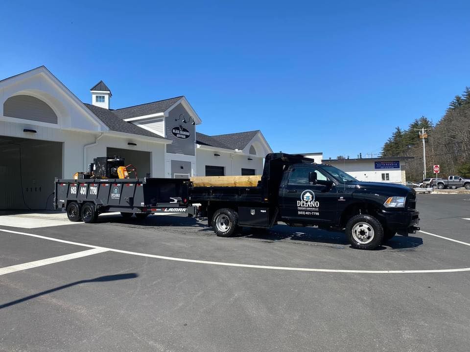 Black work truck towing a trailer on a sunny day; parked in front of a building.
