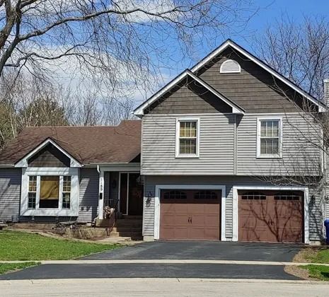 Two-story house with gray siding, brown garage doors, and a dark brown roof.