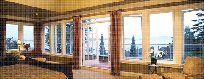 Bedroom with large windows, open French doors, overlooking a view of trees, water, and sky.