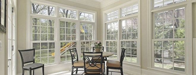 Sunroom with windows overlooking a backyard, with a table, chairs, and greenery visible through the glass.