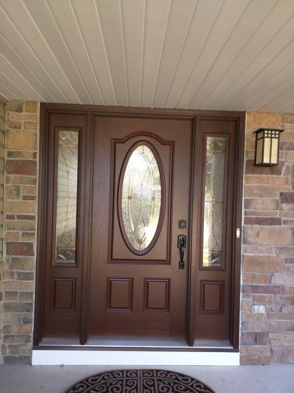 Brown front door with oval glass and sidelights, set in stone facade.