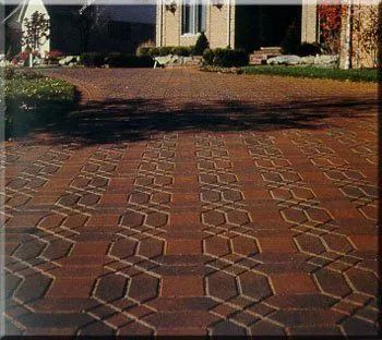 Brick driveway leading to a house with garden and shrubs in the background