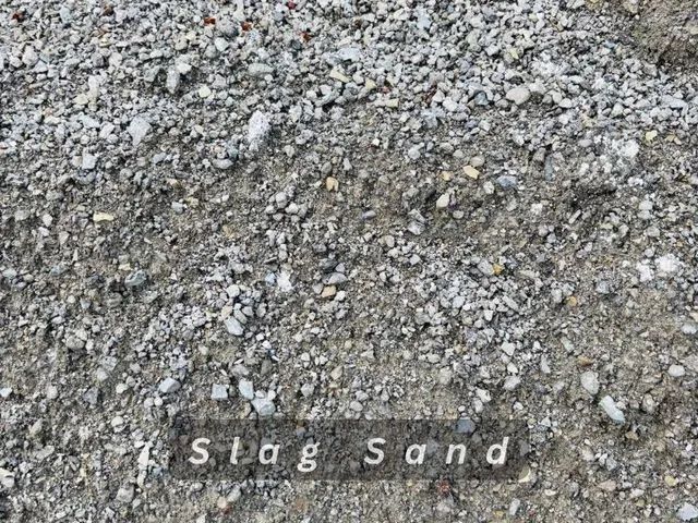 Close-up of gray and tan slag sand with the label “Slag Sand” near the bottom.