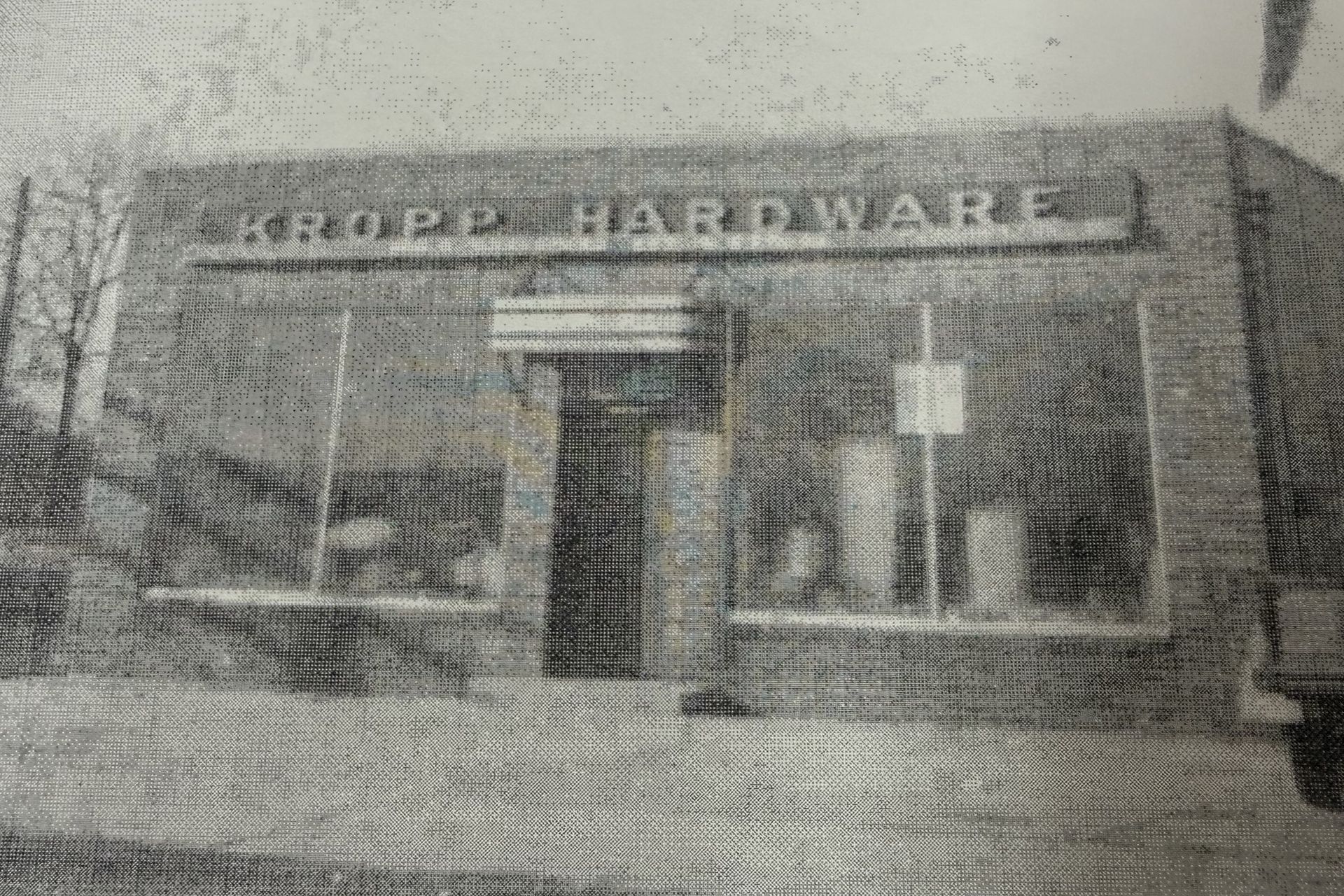 A black-and-white, grainy photo of Kropp Hardware, a brick storefront with a centered entrance and display windows.