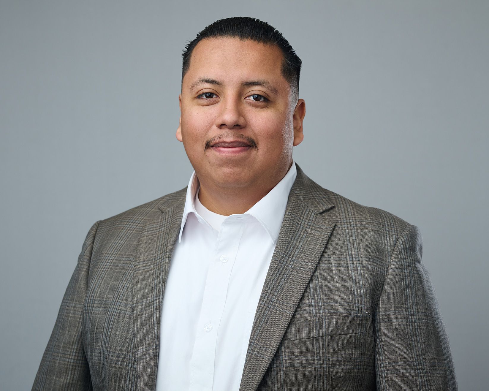 A man in a suit and white shirt is standing in front of a gray background.