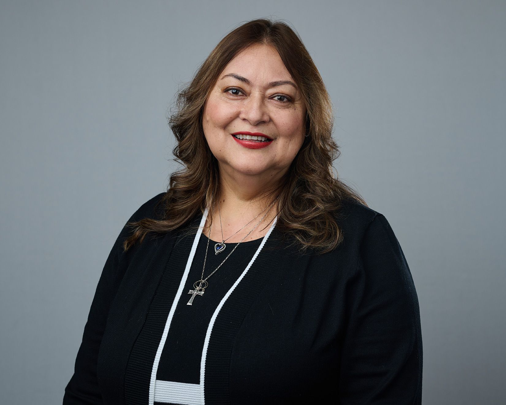 A woman wearing a black sweater and a cross necklace is smiling for the camera.