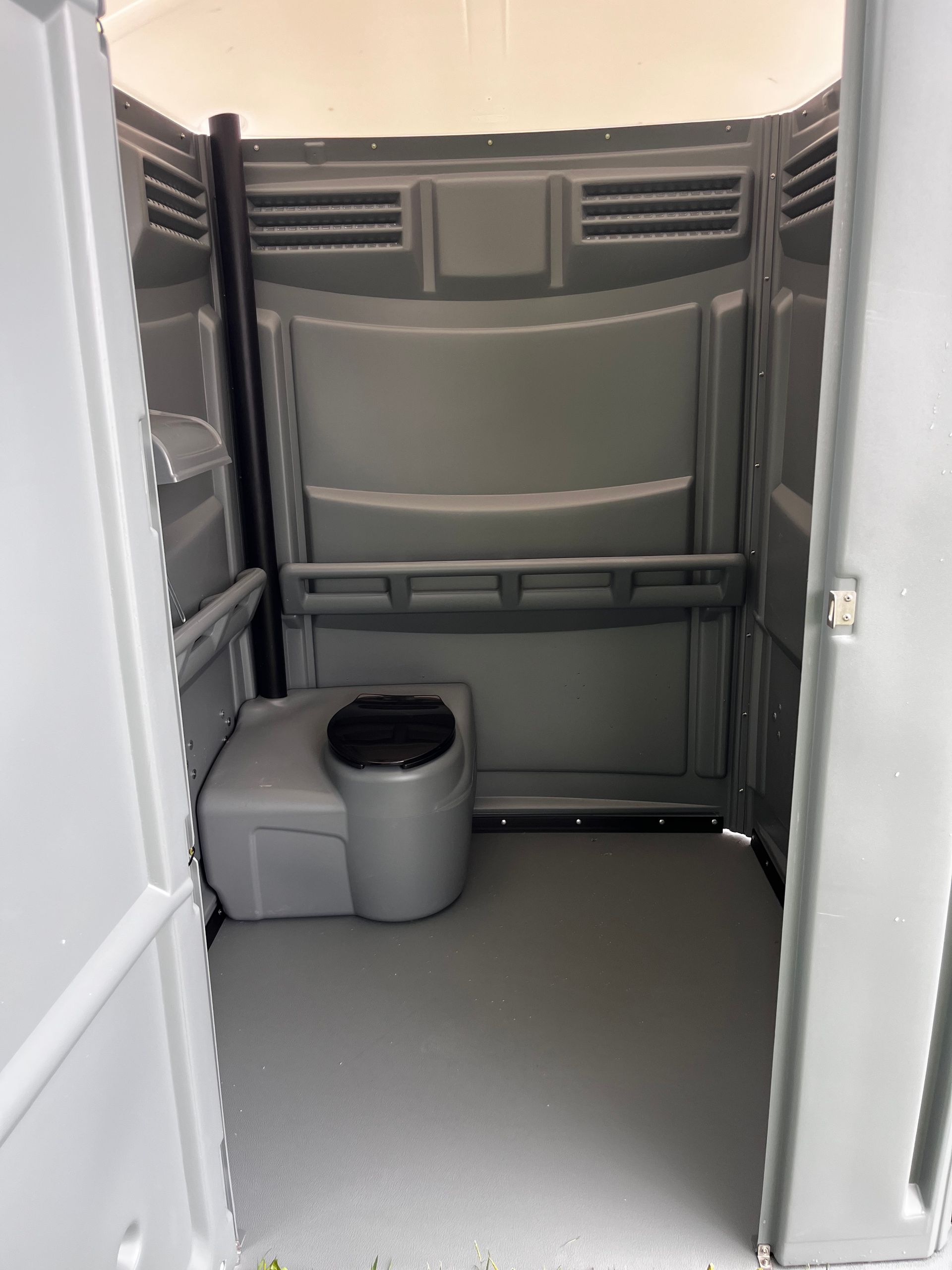 Portable restroom interior with gray walls, toilet, and open door.