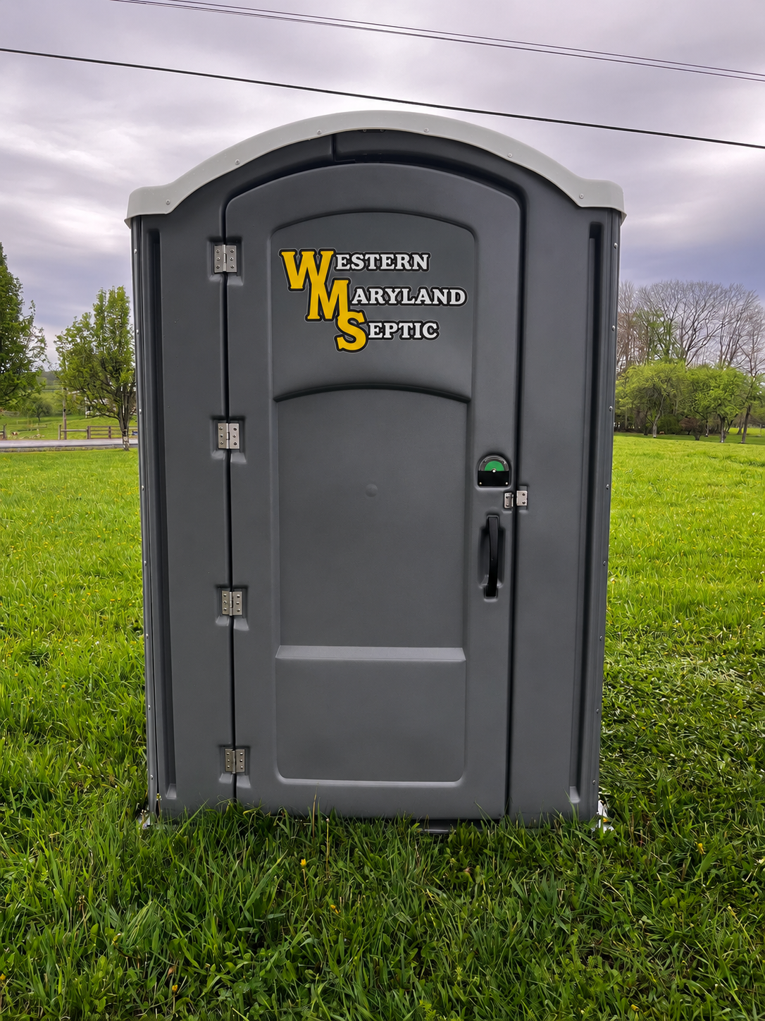 Gray portable toilet with Western Maryland Scenic logo on a grassy roadside.