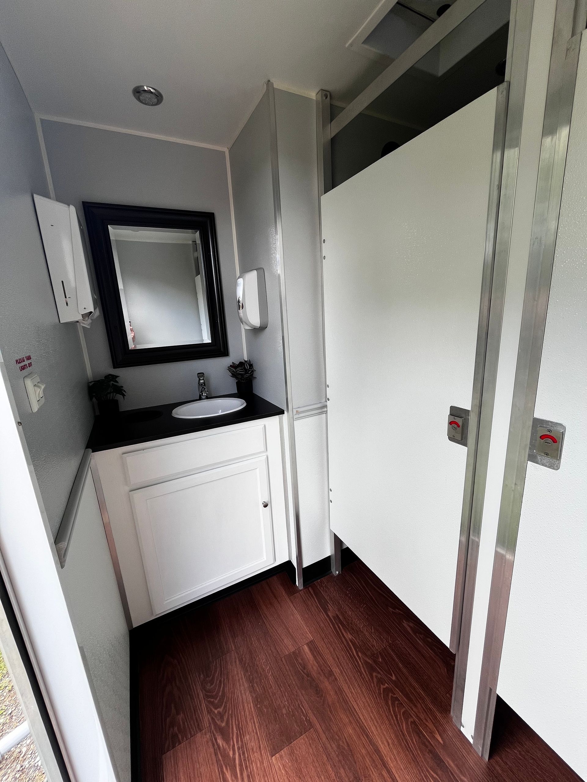 Narrow bathroom with sink, mirror, toilet, and shower stall; dark wood floor and gray walls.