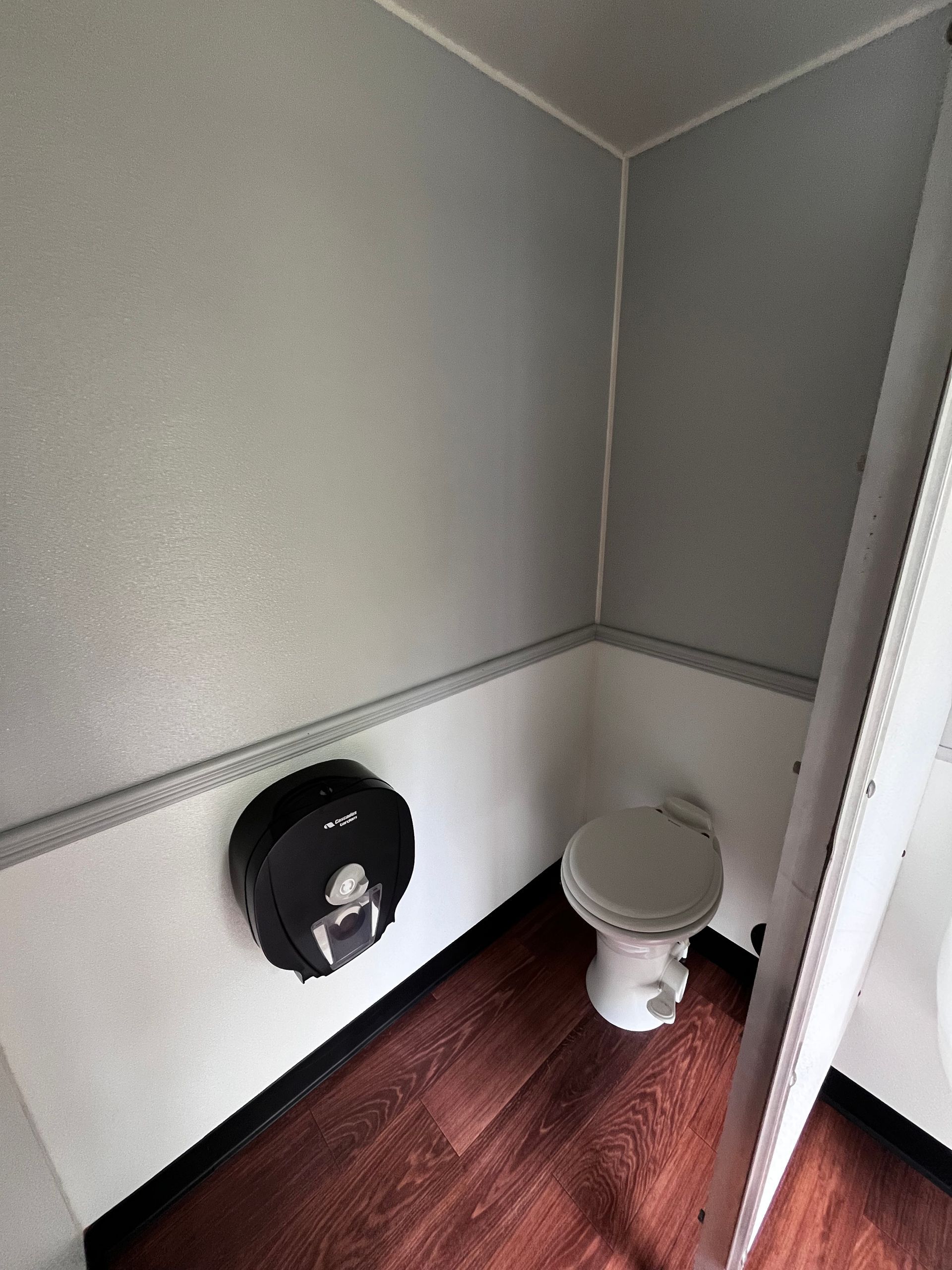 Small restroom corner with a toilet and black toilet paper holder against gray and white walls.