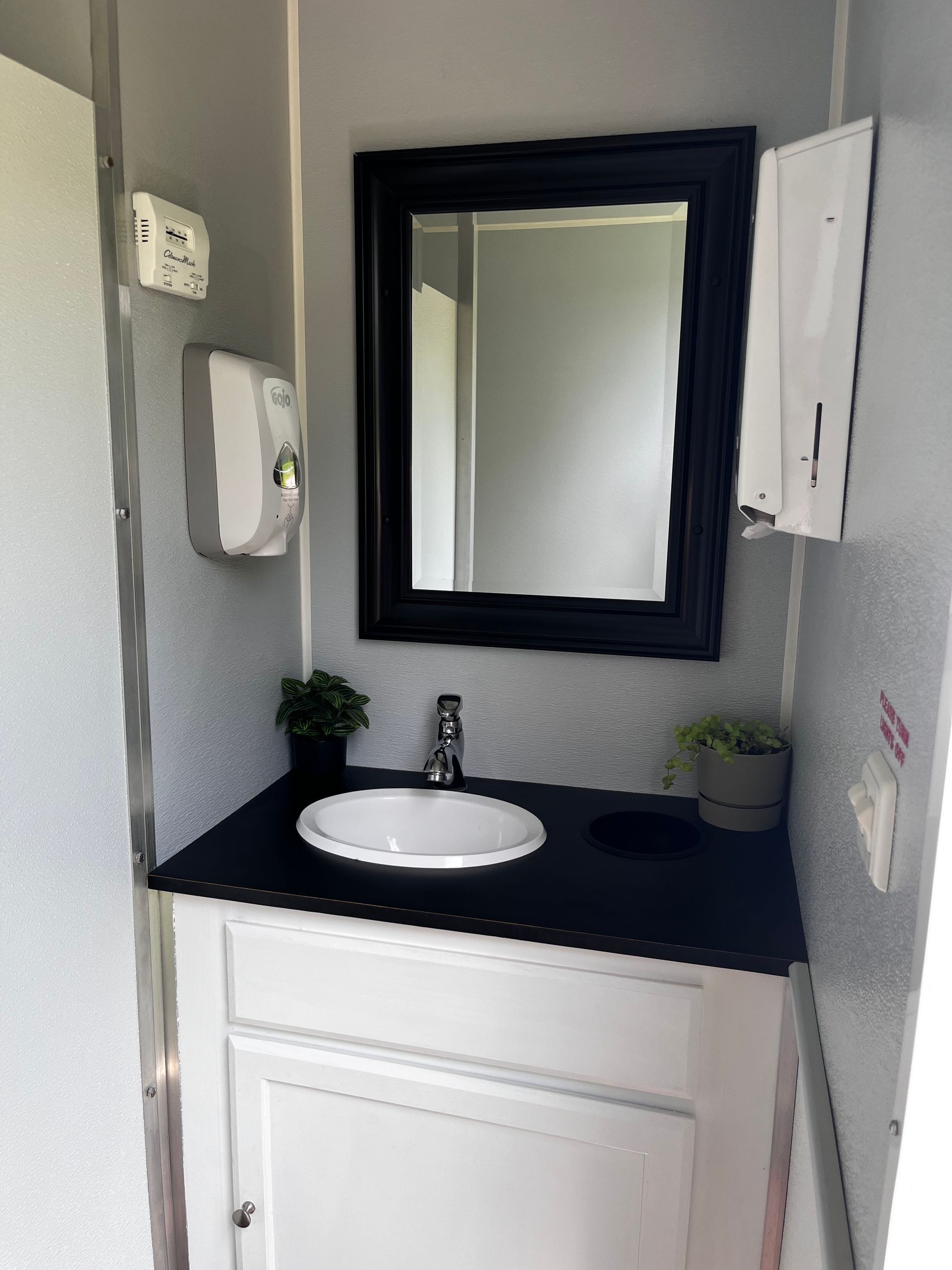 Small bathroom vanity with white sink, black countertop, mirror, and wall-mounted soap dispenser.