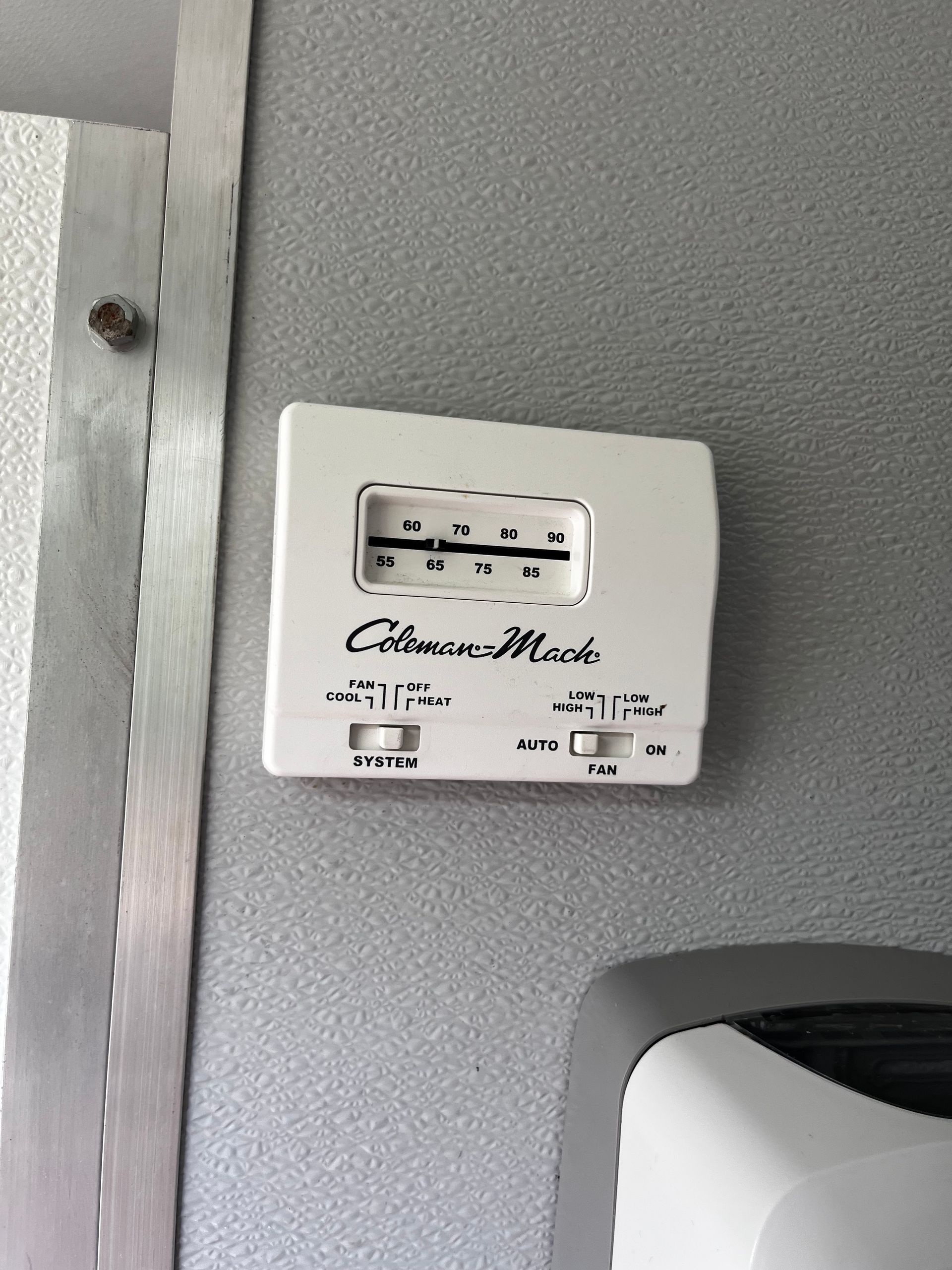 White wall-mounted control panel with a small display and labels on a gray wall.