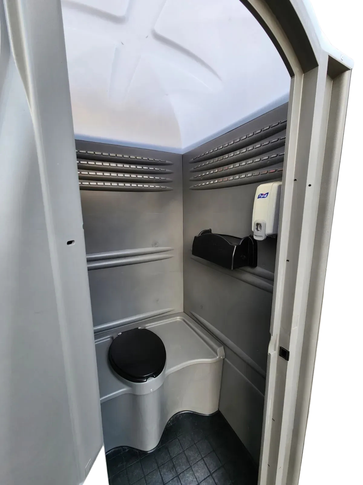 Interior of a small portable toilet stall with a white toilet and gray walls, viewed from the doorway
