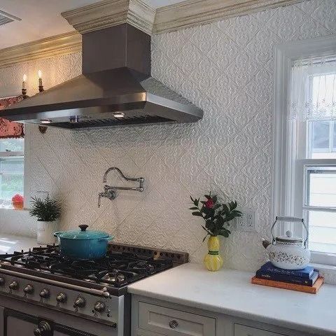 Kitchen with stainless range hood, blue pot on stove, white counters, and a small flower vase by the window