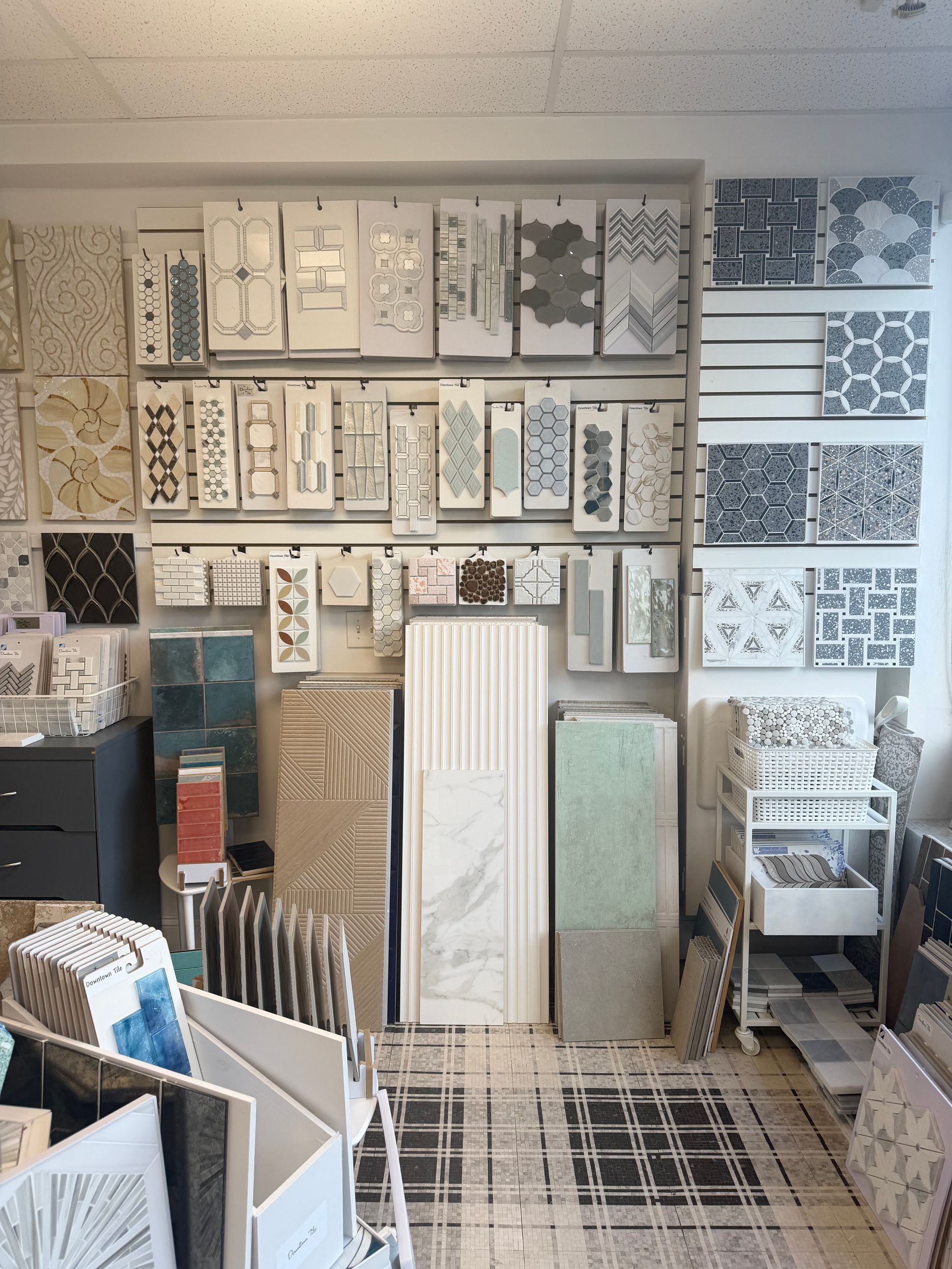 Tile and flooring showroom with display boards, patterned tiles, and sample racks arranged on shelves and floor.