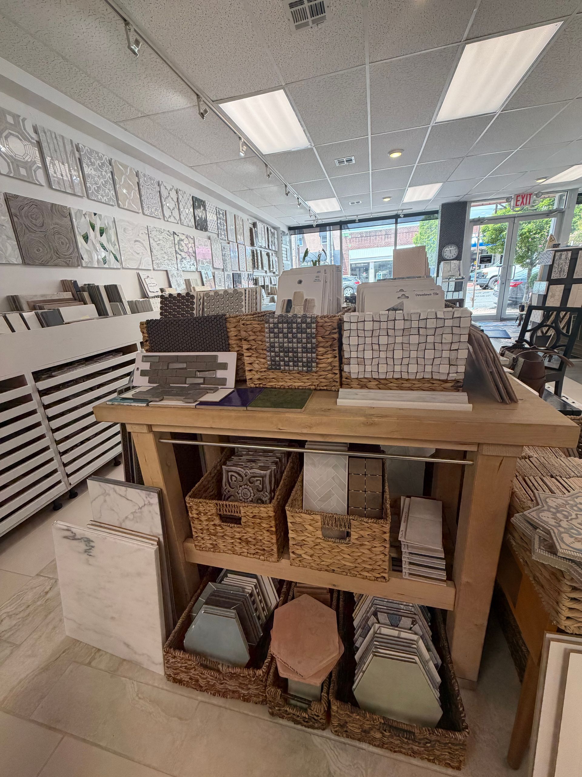 Store interior with wooden display table holding woven baskets and boxes under bright ceiling lights.
