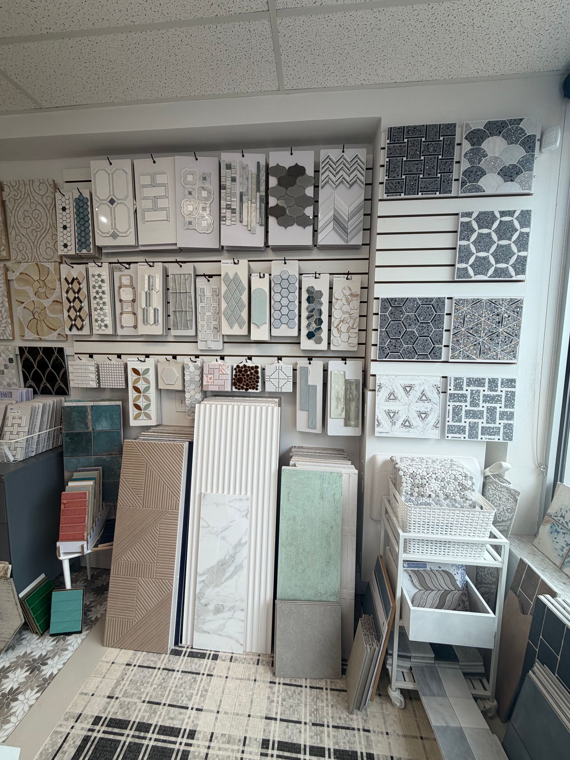 Tile showroom wall with patterned sample boards and stacks of floor tiles.