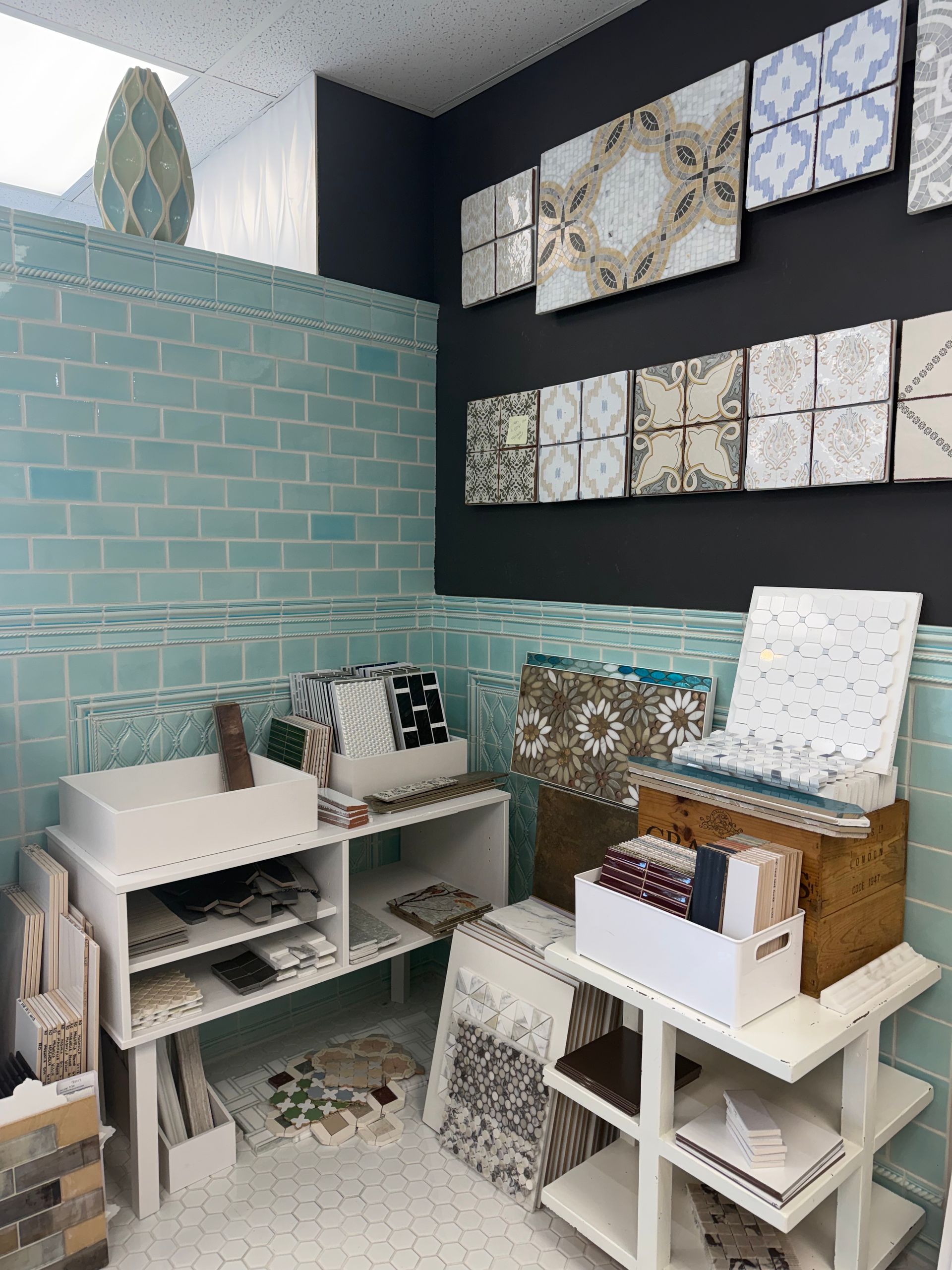 Small tile showroom with wall-mounted sample boards, a bench, and stacked decor displays.