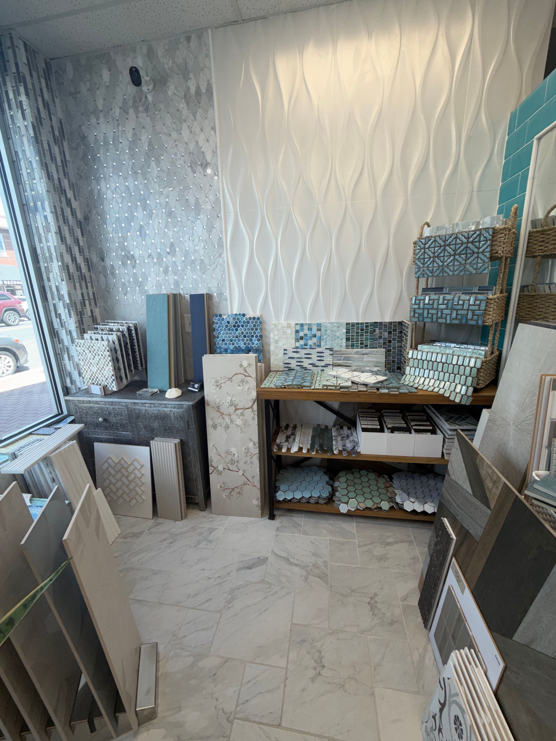 Small tiled showroom with sample boards, cabinets, and textured wall panels near a window