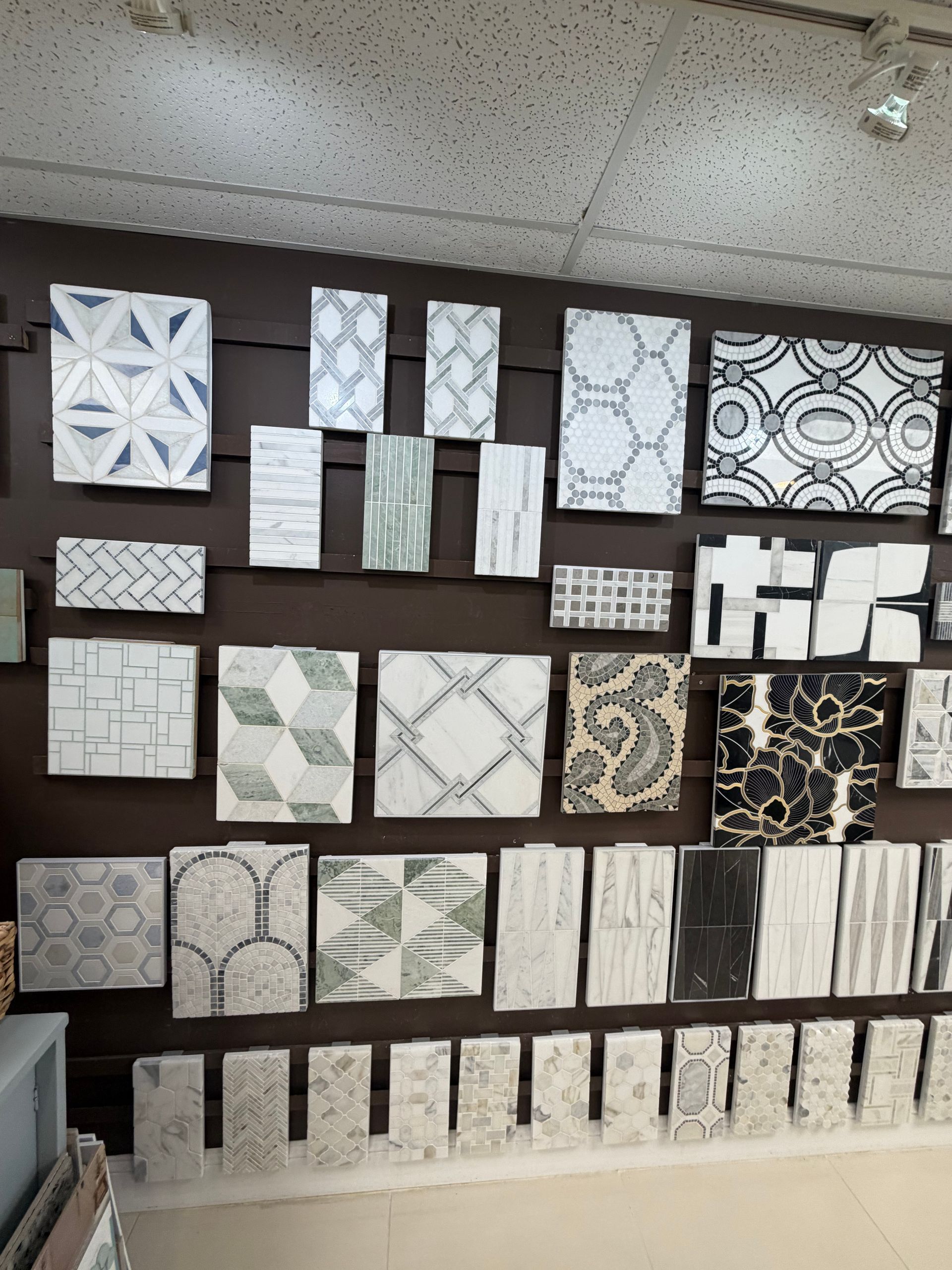 Wall display of assorted decorative tile samples in white, gray, and black patterns.