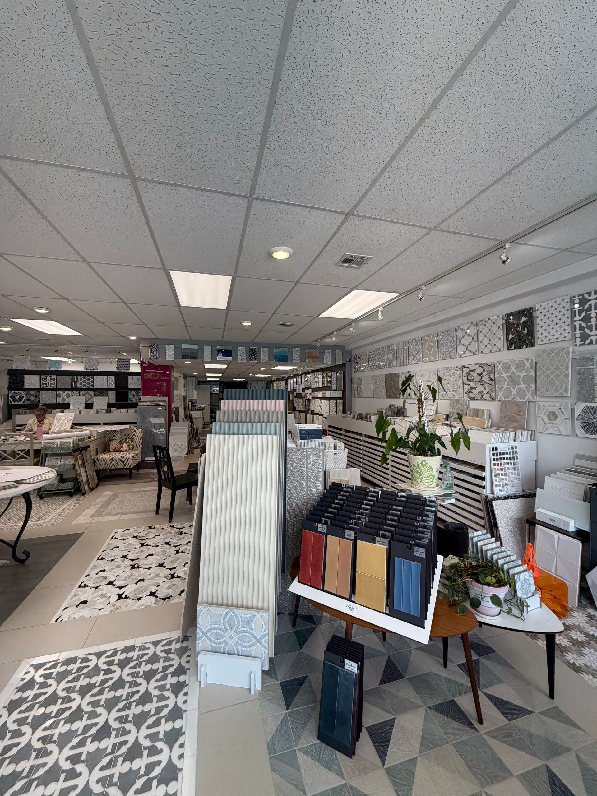 Bright modern office with desks, shelves of books, plants, and patterned flooring under a drop ceiling