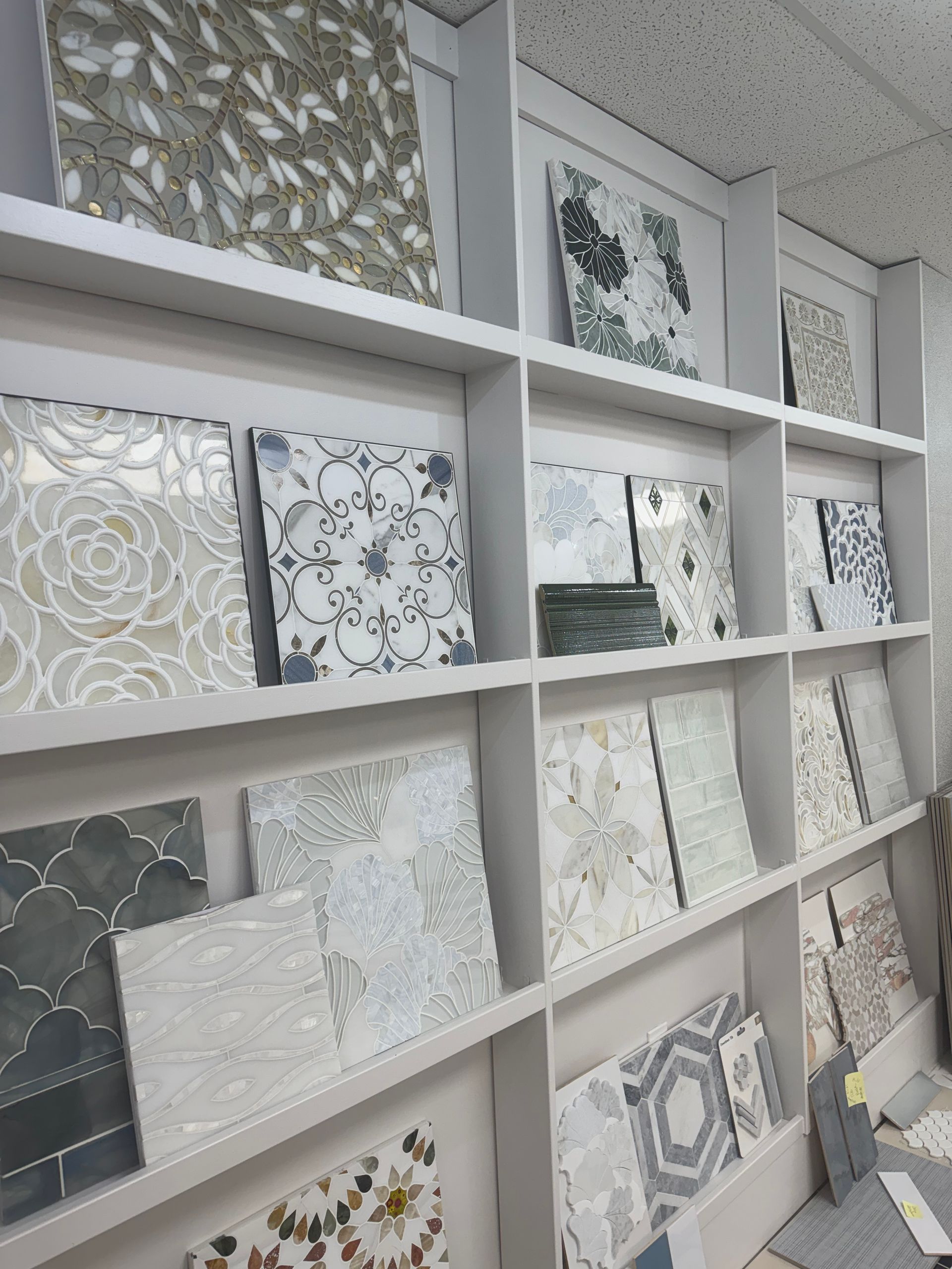 Wall of decorative tile samples in a showroom, featuring white, gray, and patterned designs