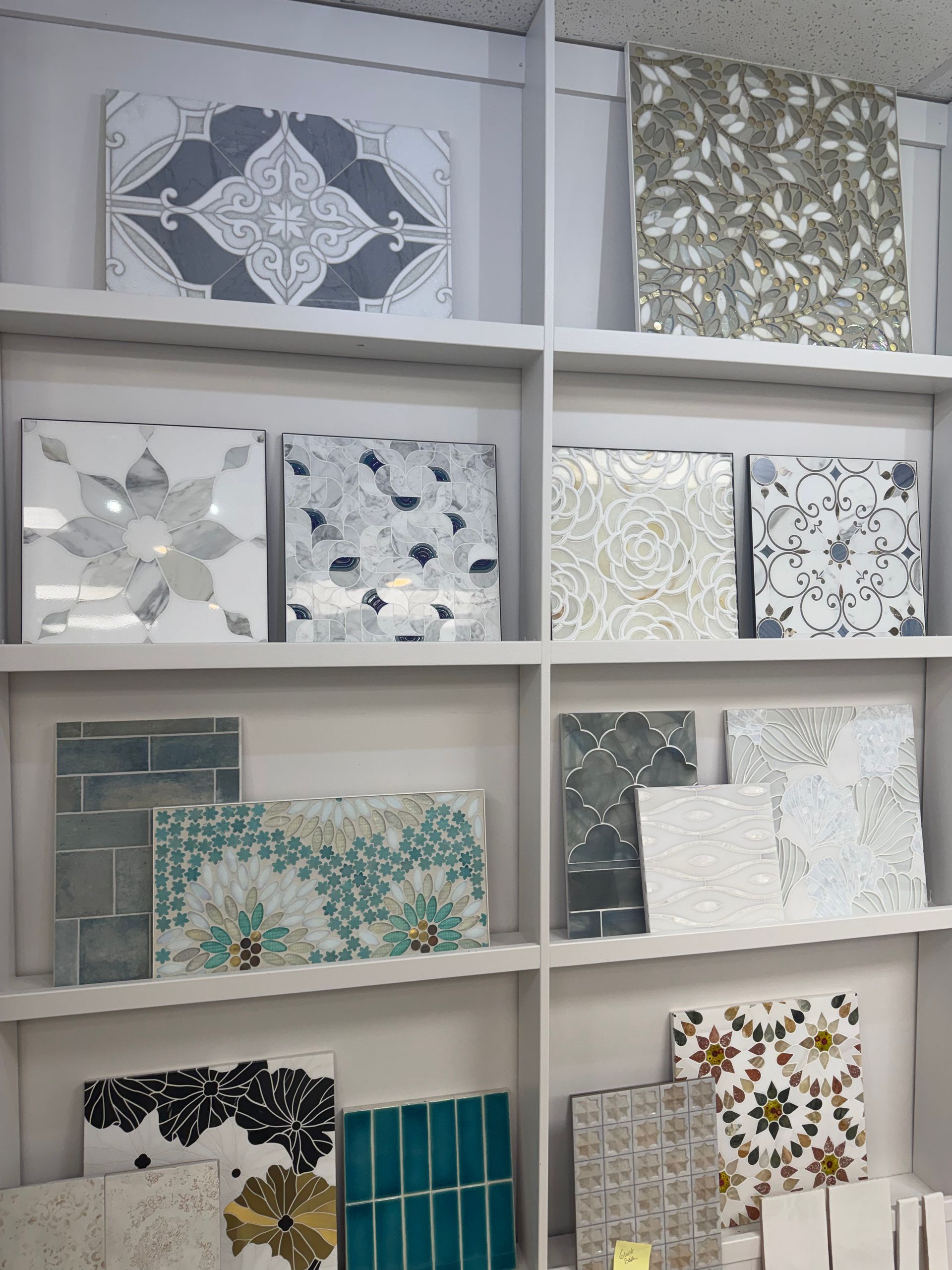 Shelves displaying assorted decorative tile samples in gray, white, teal, and floral patterns