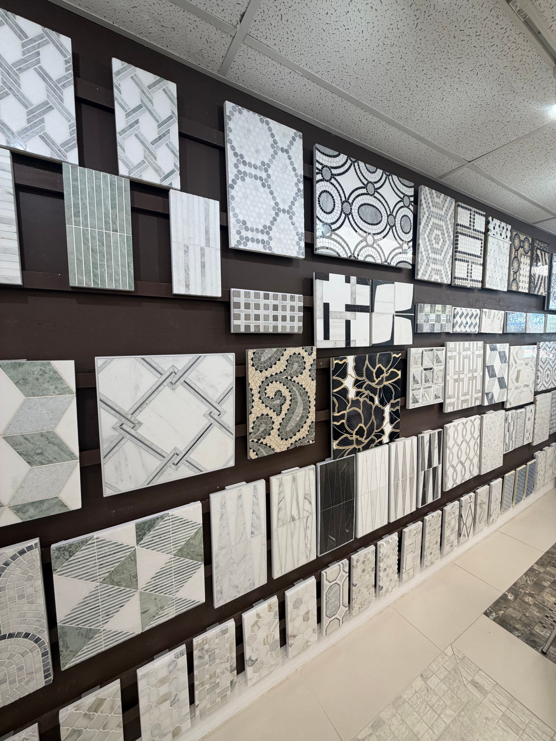 Tile display wall with assorted gray, white, and black patterned samples in a showroom