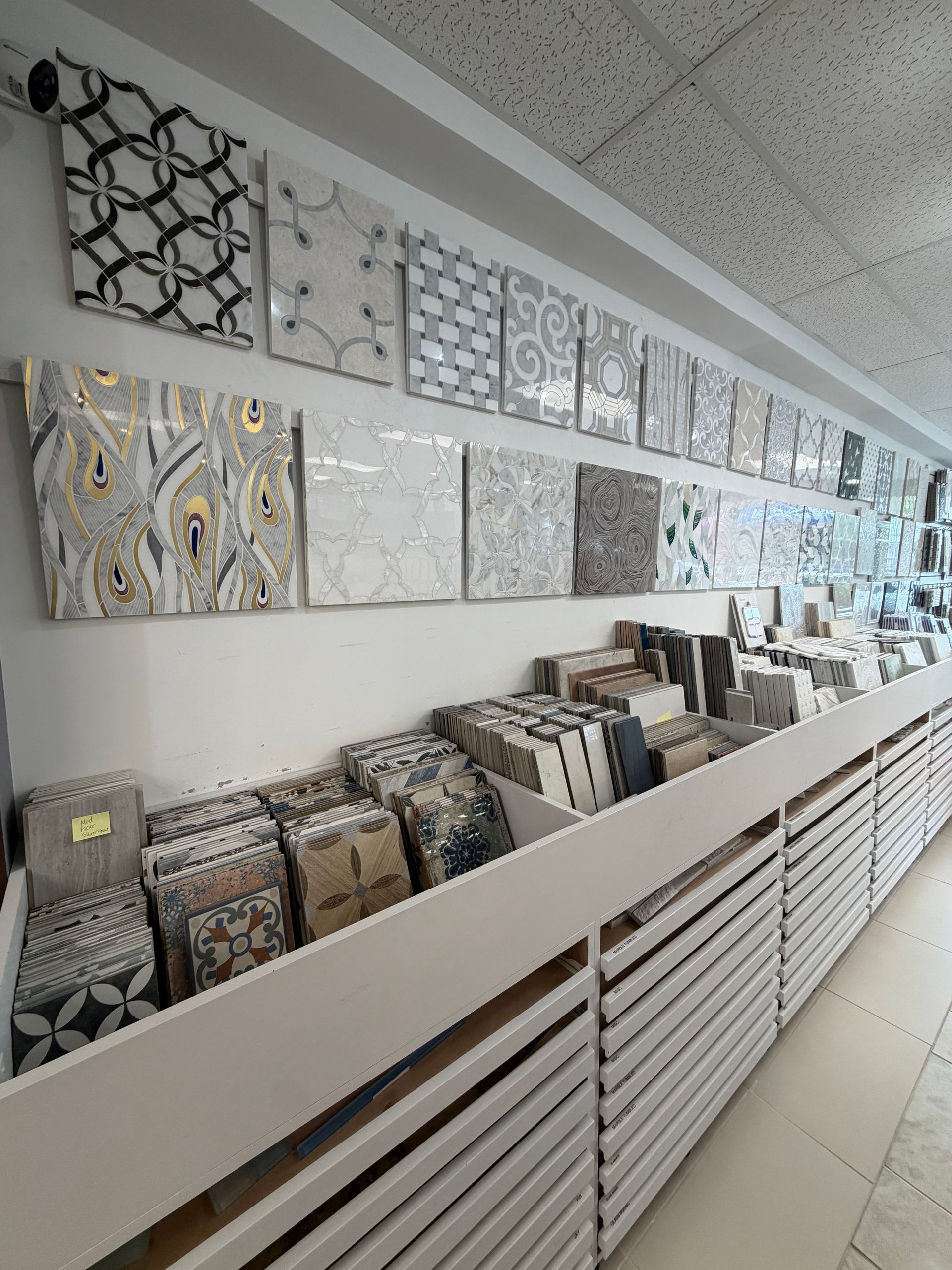 Tile and mosaic samples displayed on wall shelves in a showroom, in neutral colors and patterns